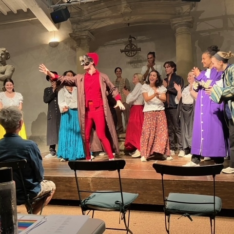 Three Commedia dell'Arte students pose on a stage wearing traditional Commedia masks and colorful costumes.